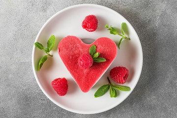 Valentines day dessert. heart shaped raw vegan red cake with raspberries and mint in a plate. healthy delicious food