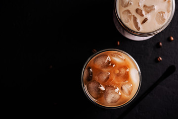 Iced coffee in a two glass with ice cubes on black concrete background, copy space,top view