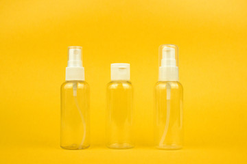 Empty cosmetic plastic bottles with pump and spray for shampoo and gel on yellow background. Clear cosmetic containers kit for travel. Template, mockup for advertising, web, social media. Stock photo.