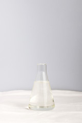 Glass transparent flask with water on a white tablecloth and with a blue background. Vertical photo with plenty of space for text input at the top. Minimalism.