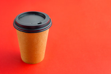 Paper coffee cup for takeaway drinks on red background with copy space. Mockup brown paper cup