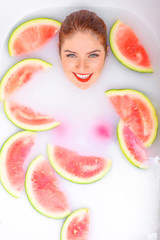 Portrait of a beautiful red-haired woman takes a bath with milk and slices of watermelon. Spa treatment for skin rejuvenation and nutrition. Ripe slices of the largest berry.