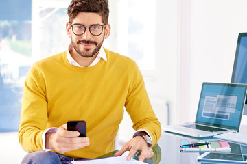 Businessman sitting at office desk and text messaging while working on laptop