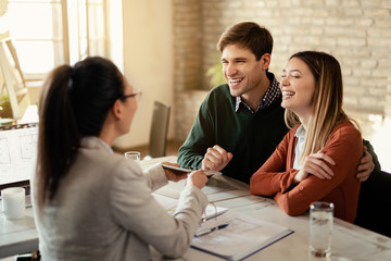 Happy couple talking to insurance agent while using touchpad in the office.