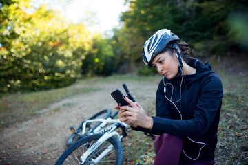 Female cyclist resting and using phone