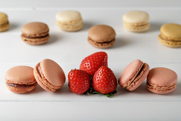 Tasty french macarons with strawberries  on white wooden board