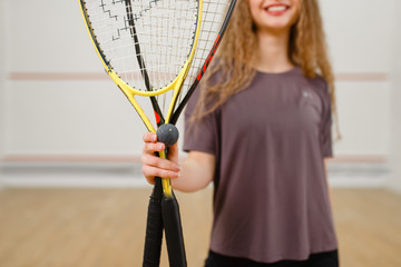 Female person shows squash racket and ball