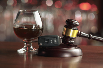 The concept of a DUI. Law hammer, alcohol and car keys on wooden table, dark background