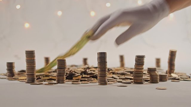 The concept of money. Columns of gold coins in the form of skyscrapers or Stonehenge. Close-up hands make up stacks of coins. Smoke. Garland.