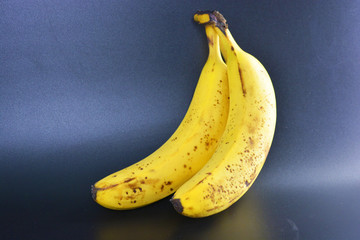 Sweet ripe yellow bananas, a bunch of three bananas with black pegmet spots are located on a black plastic background. Proper nutrition, healthy tasty fruits for every day.