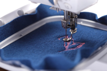 embroidery hoop of a sewing machine with boiled wool in trendy classic blue color on which a light pink magnolia embroidery is stitched- background and foreground blanked out blurry