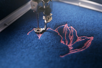 Closeup on embroidery of a light pink magnolia on classic blue boiled wool being made by a modern...