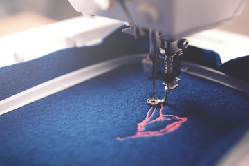 Closeup on embroidery progress of pink magnolia on boiled wool in trendy classic blue color in moody light - background and foreground blanked out blurry