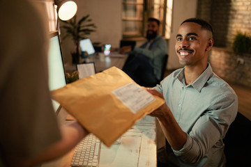 Happy black entrepreneur receiving package from delivery person while working in the office.