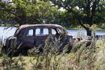 Rusting and old car in a field by a pond