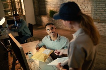 Happy black businessman receiving delivery and signing to a courier in the office.