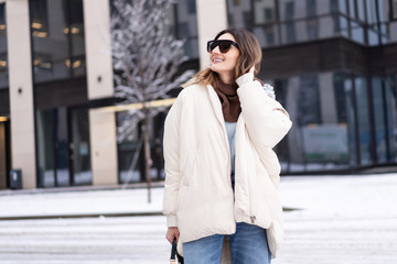 European model in a beige oversized down jacket, knitted sweater with a handbag and glasses posing...