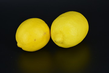 Large, ripe bright yellow two lemons lie on a black plastic background. Delicious and sour fruits, healthy food for every day.