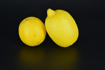 Large, ripe bright yellow two lemons lie on a black plastic background. Delicious and sour fruits, healthy food for every day.