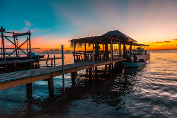 Obraz premium Sunset on a pier and the boat in the background on a beach on Roatan Island. Honduras