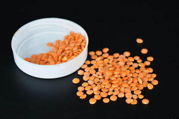 Grains, seeds of red lentils, a handful of lentils are located and scattered in a white plastic cover on a black plastic background.