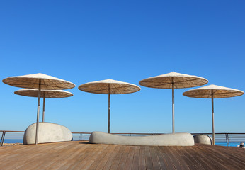 Tropical sun umbrellas of reed and straw  on wooden promenade opposite the sea coast against a bright blue sky on a sunny summer day. Beach sunshades. Travel and vacation. Ecotourism. 