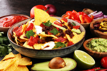 mexican nacho chips garnished with ground beef, guacamole, melted cheese, peppers and cilantro leaves in plate