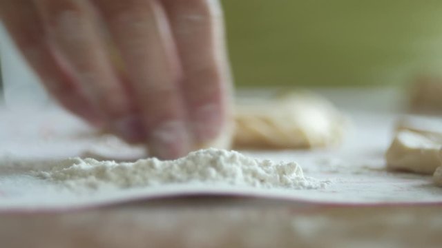 unrecognizable woman is heaping round pieces of a dough in a flour for making dumplings, 4K close-up