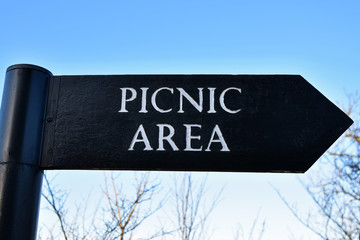 Picnic area sign with arrow pointing right. On wooden board with blue sky and branches in background. Taken next to Wallace Monument in Stirling, Scotland.