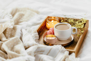 Obraz na płótnie Canvas Wooden tray of coffee and candles on bed. White bedding sheets with striped blanket and pillow. Breakfast in bed. Hygge concept.