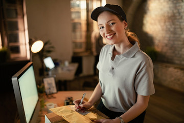 Young happy courier preparing packages for delivery in the office.