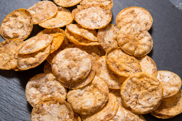 Top view pile of organic, crispy, baked, whole grain rice chips with spices. Gluten free healthy snack. On black sliced stone background