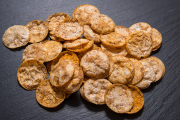 Top view pile of organic, crispy, baked, whole grain rice chips with spices. Gluten free healthy snack. On black sliced stone background