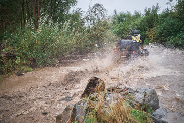 Quad rider jumping on a muddy forest trail.