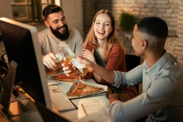 Team of happy freelance workers toasting with beer while eating pizza in the office.