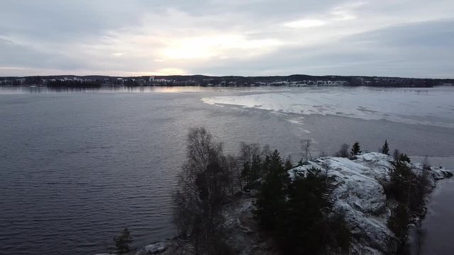 Drone aerial shot, rising backwards, of partly frozen Pyhajarvi lake in Tampere, Finland on a cloudy and windy winter day at sunset