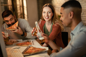 Happy creative woman drinking beer and eating pizza with her coworkers in the office.
