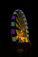 Monument of August the Strong in front of a turning, glowing Ferris wheel during the Christmas market in Dresden