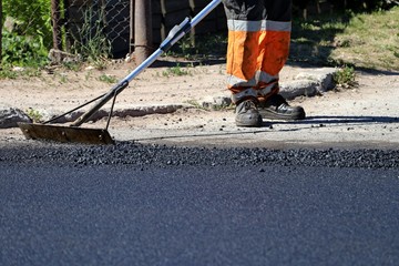 Worker using tool to smooth asphalt on driveway. Road repairing.