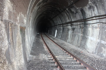 Obraz premium dark black shaded tunnel in an underground tunnel in a cavern of a railway along the tracks of a train towards the station