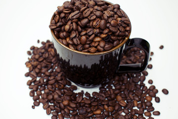 Close up on dark coffee mug overflowing with whole coffee beans