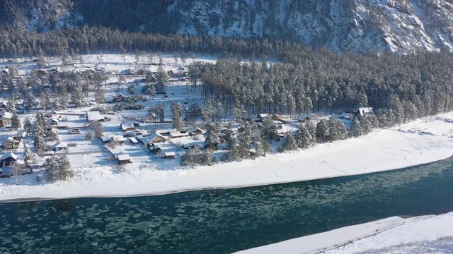 Siberian village in the snow on the shore of a turquoise mountain river aerial view
