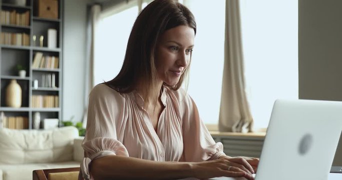 Smiling attractive young woman typing on laptop sit at table