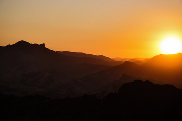 The sun sets behind the distant mountain ridges and illuminates them with its evening light.