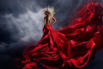 Fototapeta premium Kobieta w czerwonej sukience tańczy nad burzowym niebem, trzepotliwy materiał sukni latający jak plusk