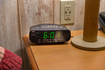 A nightstand with a tabletop lamp, alarmclock, and touchtone phone