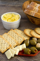 Delicious Snack, Crackers, Olives, Butter, Cheese and Bread in a Basket on Wood Table