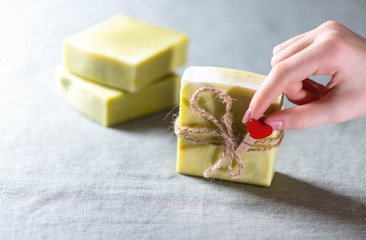 Natural handmade soap with a heart decor on a background of linen fabric. Children's hands hold natural soap.