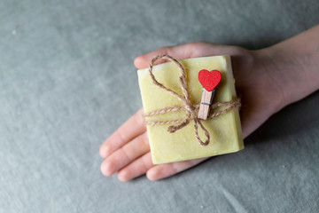 Natural handmade soap with a heart decor on a background of linen fabric. Children's hands hold natural soap.