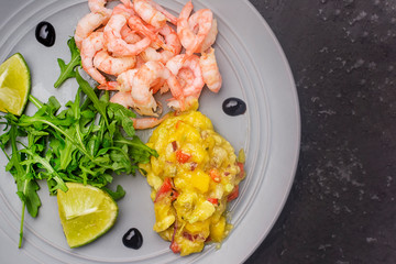 On a gray plate are shrimp, mango chutney sauce and arugula salad. Photo above. Copy space.